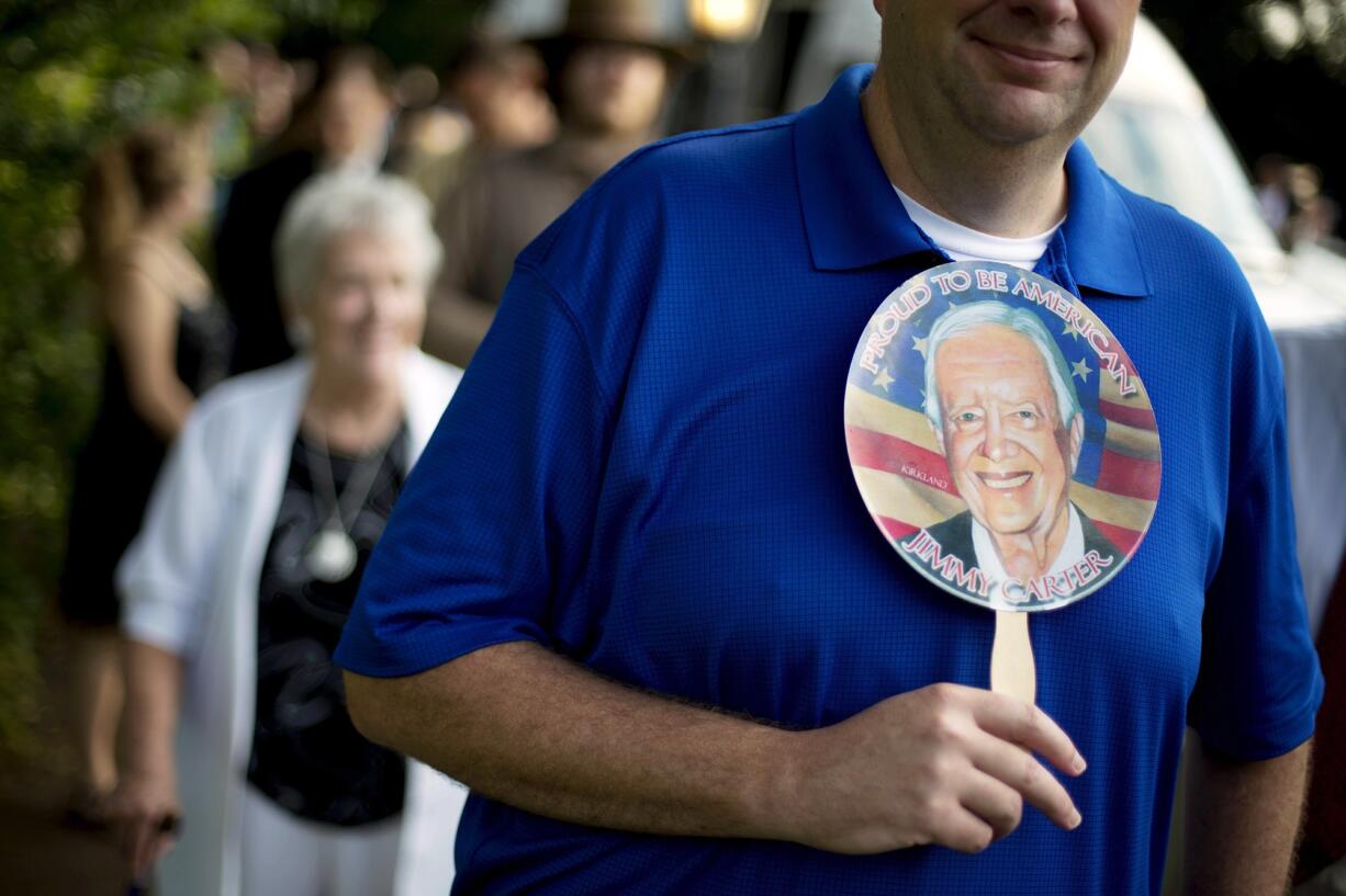 Bill Case, of Columbia, S.C., holds a fan bearing the image of former President Jimmy Carter while waiting in line to enter Maranatha Baptist Church for Sunday School class Sunday in Plains, Ga.