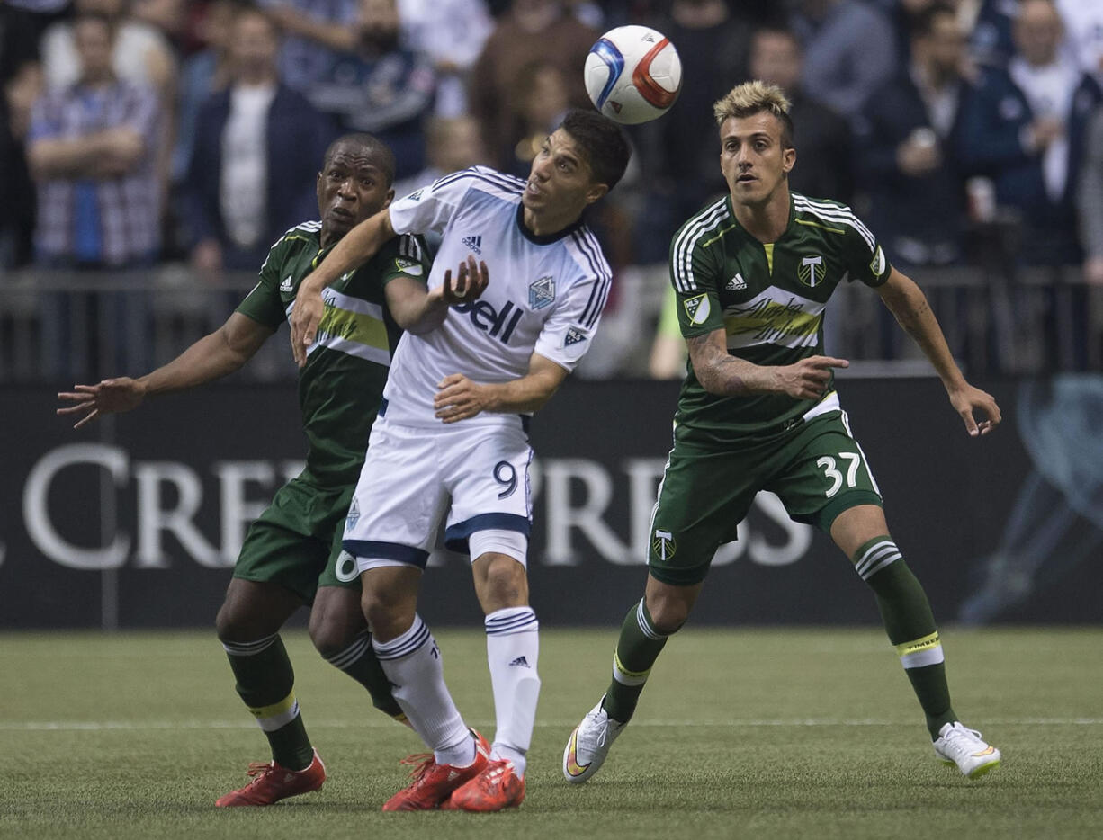 Vancouver Whitecaps FC Nicolas Mezquida, center, fights for control of the ball with Portland Timbers Darlington Nagbe, left, and Maximiliano Urruti during the first half of a MLS soccer match, Saturday, March 28, 2015 in Vancouver, British, Columbia.