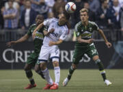 Vancouver Whitecaps FC Nicolas Mezquida, center, fights for control of the ball with Portland Timbers Darlington Nagbe, left, and Maximiliano Urruti during the first half of a MLS soccer match, Saturday, March 28, 2015 in Vancouver, British, Columbia.