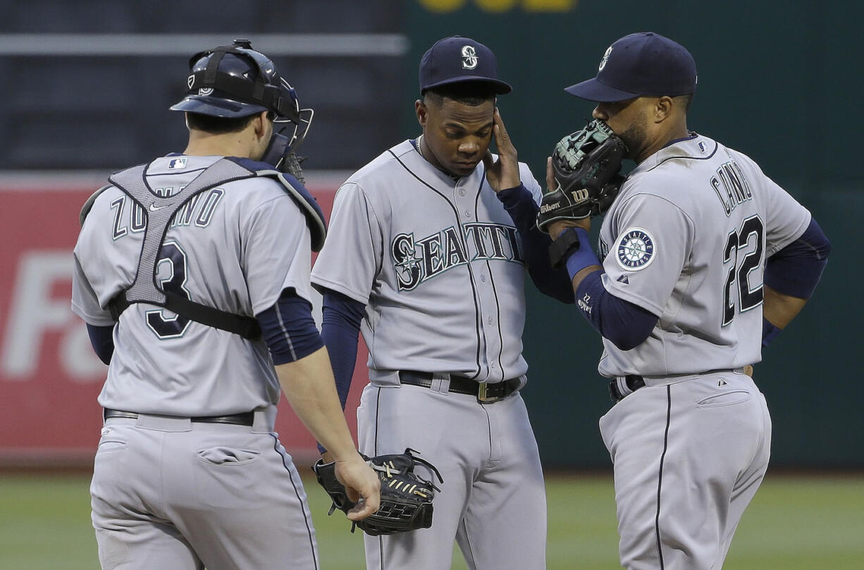 Seattle Mariners pitcher Roenis Elias, center, meets with catcher Mike Zunino (3) and second baseman Robinson Cano (22) during the first inning against the Oakland Athletics in Oakland, Calif., Thursday, July 2, 2015. The Athletics won 4-0.