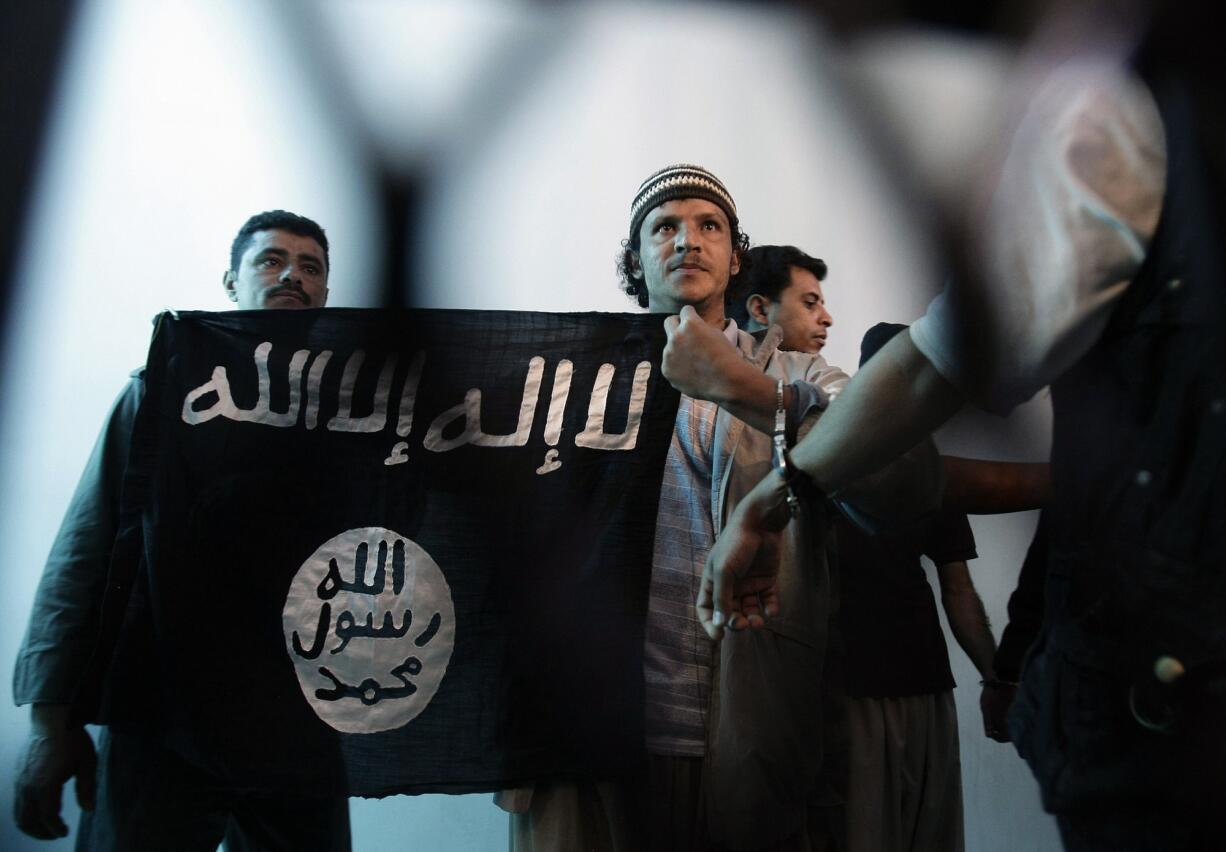 A suspected Yemeni al-Qaida militant, center, holds an Islamist banner April 23, 2013, as he stands behind bars during a court hearing in state security court in Sanaa, Yemen.