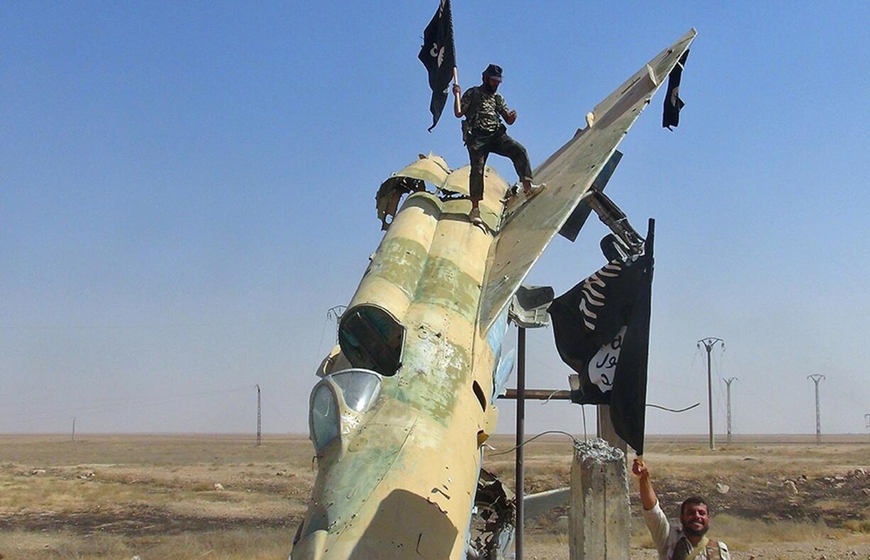 Fighters of the Islamic State wave the group's flag from a damaged display of a government fighter jet following the battle for the Tabqa air base, in Raqqa, Syria.