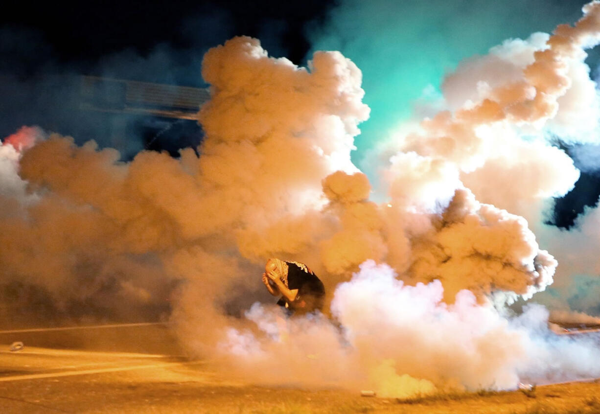 A protester takes shelter from smoke billowing around during Aug. 13 protests against the shooting of 18-year-old Michael Brown in Ferguson, Mo. Missouri police, in advance of a grand jury decision on whether to charge the white police officer who fatally shot the black teen, are making extensive preparations hoping to avoid a repeat of violent clashes between protesters and police. (AP Photo/St.