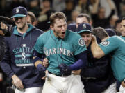 Seattle Mariners' Logan Morrison, center, emerges from a crowd of teammates who crowded around him at home after his walk-off home run against the Oakland Athletics in the 11th inning Friday, May 8, 2015, in Seattle. The Mariners won 4-3.