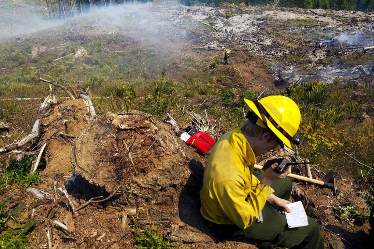 Washington State Department of Natural Resources firefighter Schuyler Jorgensen of Tenino calls in a weather report as a DNR firefighter walks down a smoking hill as crews battle the Teague Road fire west of Centralia on Monday.