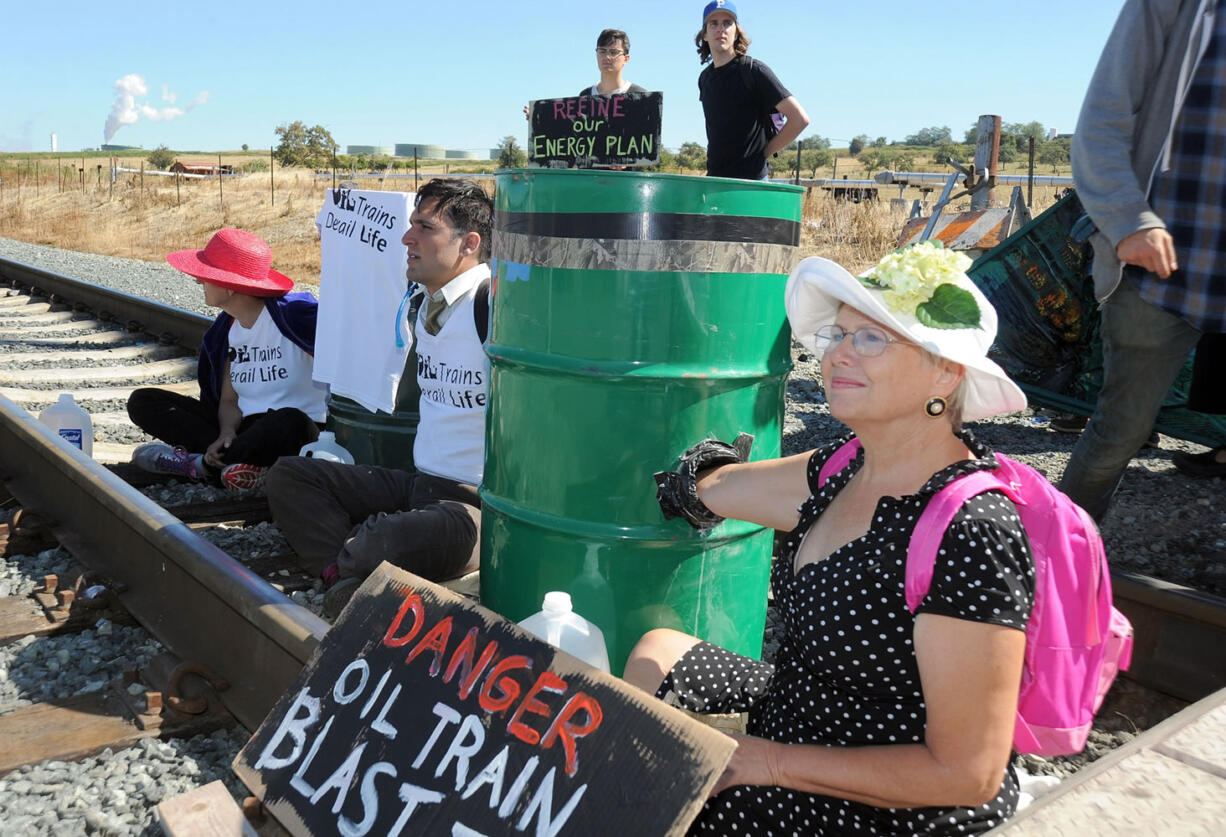 Oil train protestors, from left, Annette Klapstein of Bainbridge Island, Adam Gaya of Seattle and Jan Woodruff of Anacortes sit on the tracks at the Texas Road crossing on March's Point to block a train from leaving the Tesoro Refinery railroad yard in Anacortes on July 28.