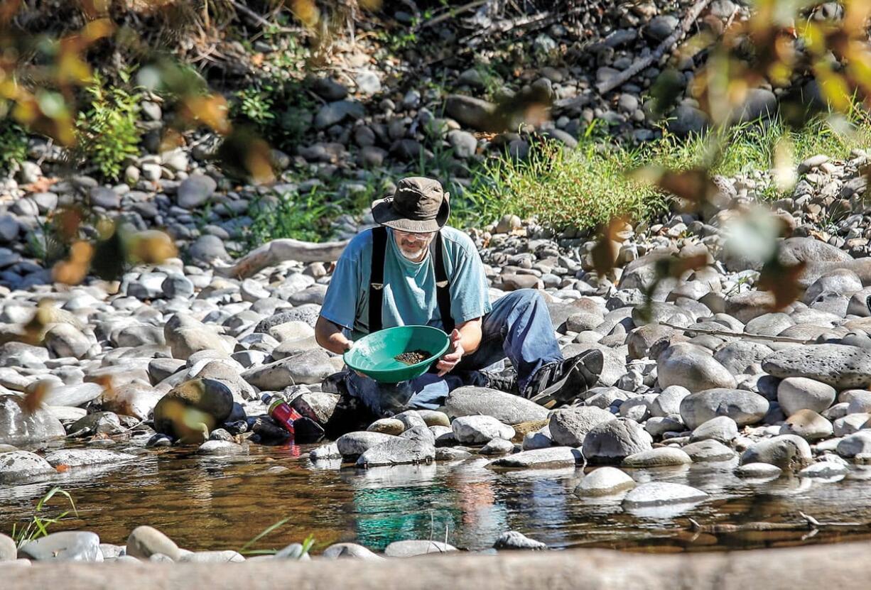 Rebecca Fuller of Troutdale, Ore., pours spoonfuls of dirt into the stream of water at the top of the angled trough on the portable sluice machine that she and her husband, Bruce, are using on the East Fork of the Lewis River to search for gold.