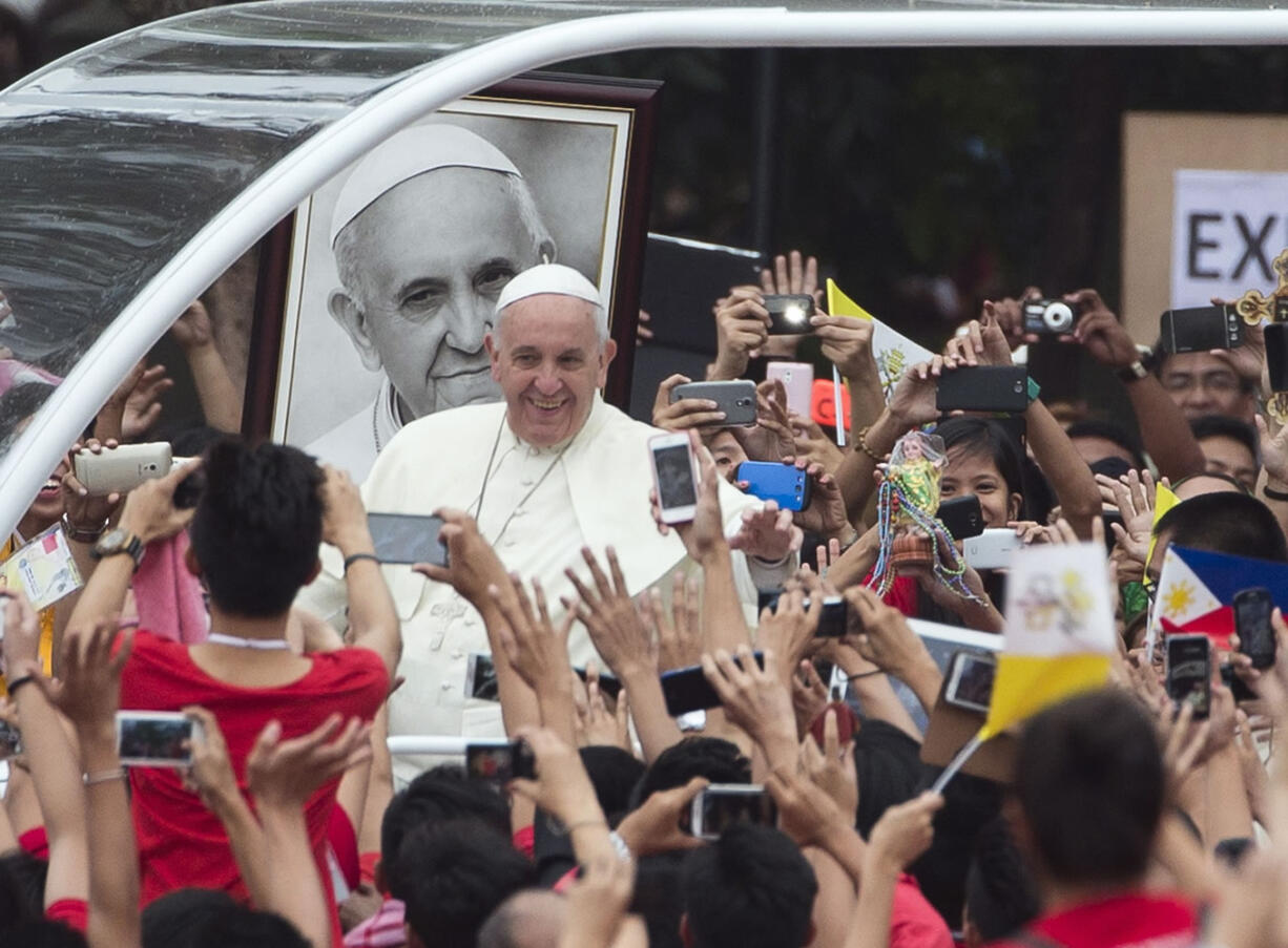 Pope Francis passes past a portrait of himself as he arrives to meet youths Sunday at Santo Tomas University in Manila, Philippines.