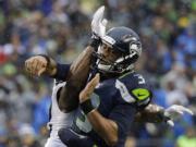 Seattle quarterback Russell Wilson gets hit by an Oakland  defensive player after Wilson got a pass off in the second half Sunday in Seattle.