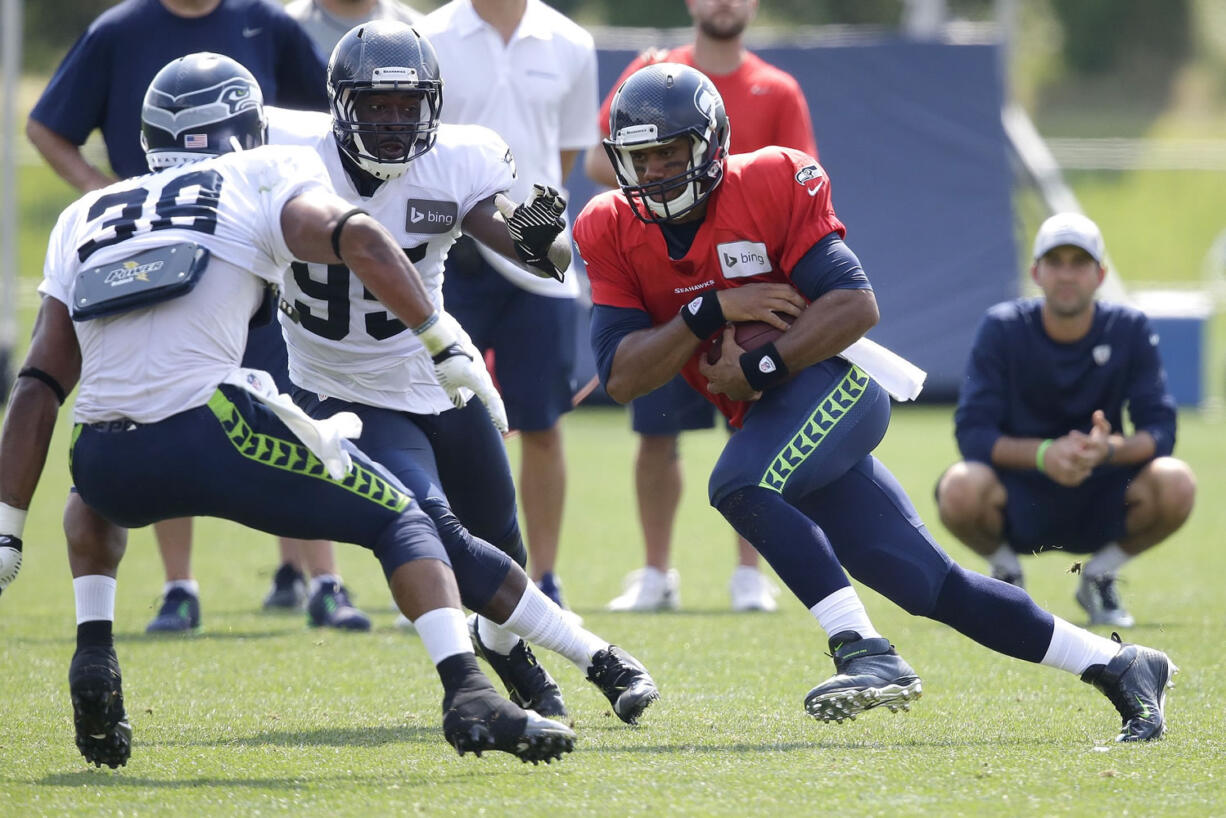 Seattle Seahawks quarterback Russell Wilson, right, keeps the ball as he tries to avoid the defense of linebacker Marcus Dowtin (38) and defensive end Benson Mayowa (95), Saturday, Aug. 2, 2014, during NFL football training camp in Renton, Wash. (AP Photo/Ted S.