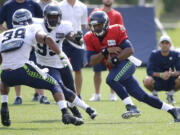 Seattle Seahawks quarterback Russell Wilson, right, keeps the ball as he tries to avoid the defense of linebacker Marcus Dowtin (38) and defensive end Benson Mayowa (95), Saturday, Aug. 2, 2014, during NFL football training camp in Renton, Wash. (AP Photo/Ted S.