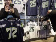 A couple of days out from the Seattle Seahawks winning the NFC championship on their way to the Super Bowl, Erin Rempel-Cheuk, left, calls her husband Tuesday in Seattle, to check on the jerseys he wants for he and his friends who will be attending the Super Bowl.