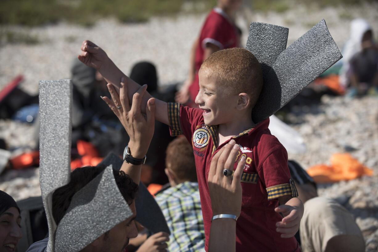 A Syrian migrant that was rescued by Turkish Coast Guard while trying to cross in boats to Greece, plays with a child with parts of their life jackets, that were destroyed by the authorities in order not to be used again, wait in Cesme, Turkey, to be taken to the nearby city of Izmir to be processed by immigration officials Wednesday.