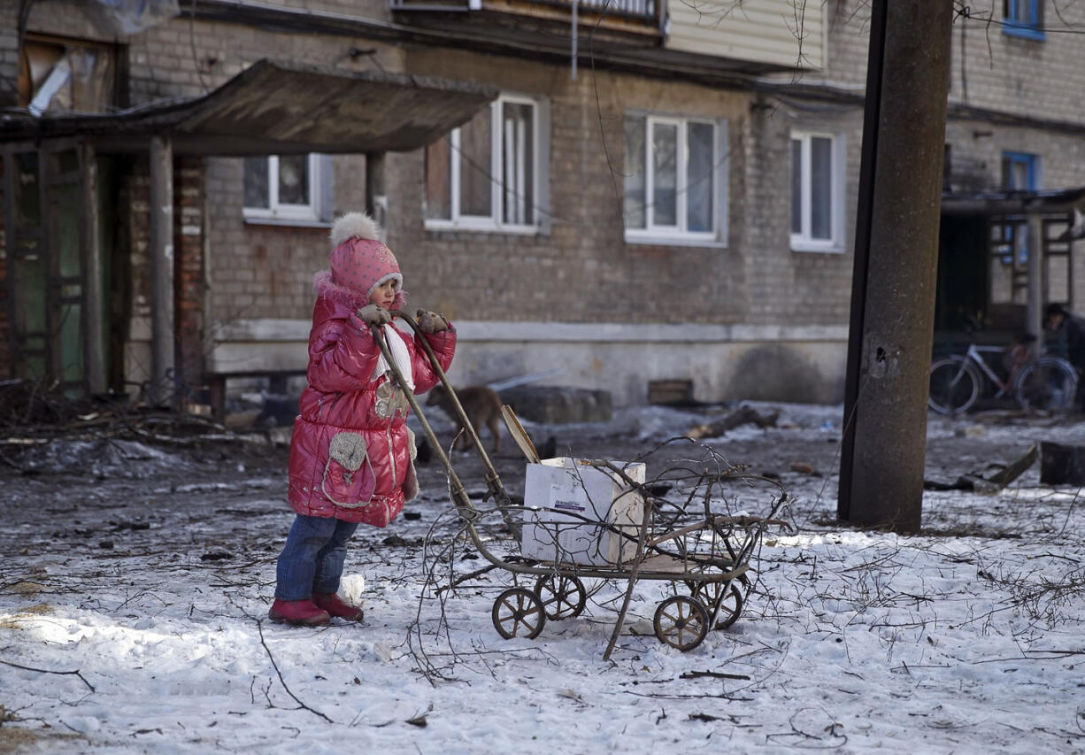 Dorina, 3, leans on a cart used to carry tree branches for firewood Friday outside a damaged apartment building in Debaltseve, Ukraine.