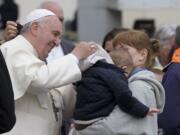 Pope Francis helps a child with a hood Wednesday as he leaves after his weekly general audience in St.