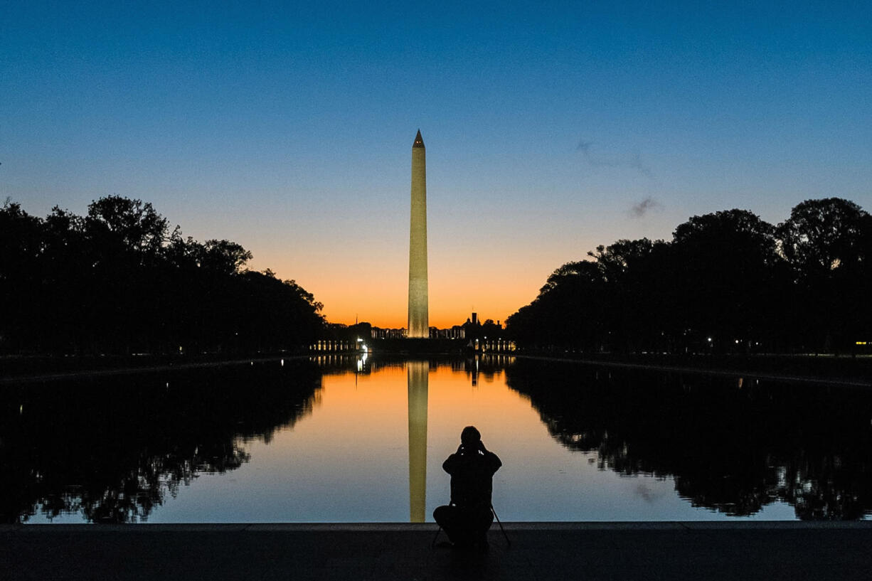 A photographer is silhouetted in the reflecting pool as he captures the sunrise behind the Washington Monument in Washington on Oct.