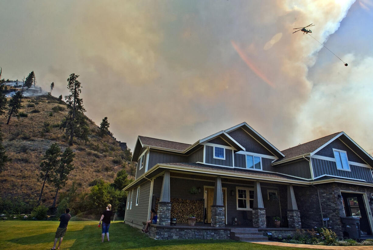 A homeowner and friend watch as helicopters put water on the Mills Canyon wildfire behind their homes near Entiat.