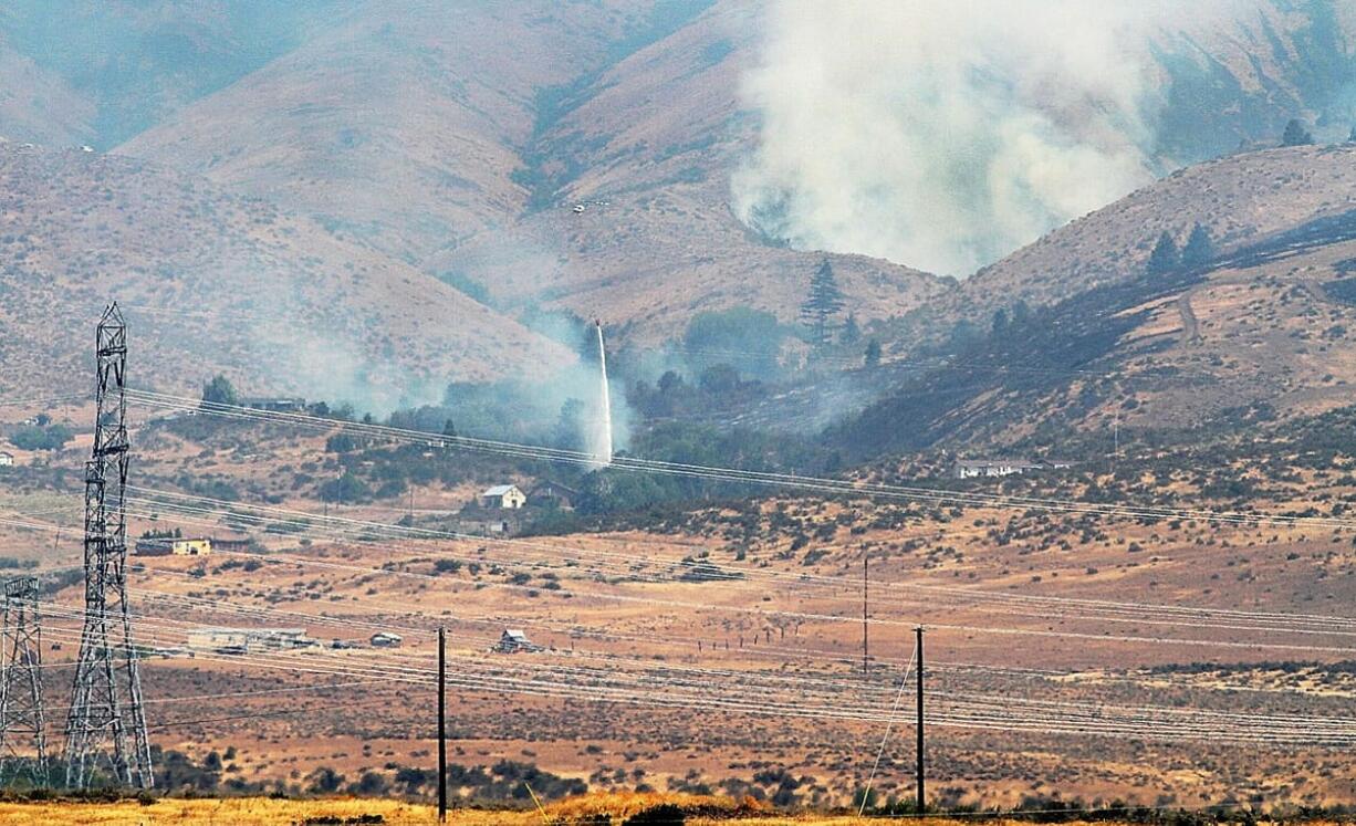 A UH-1H Huey helicopter, operated by the Washington State Department of Natural Resources, makes a water drop near homes in the Snag Canyon fire area Sunday.