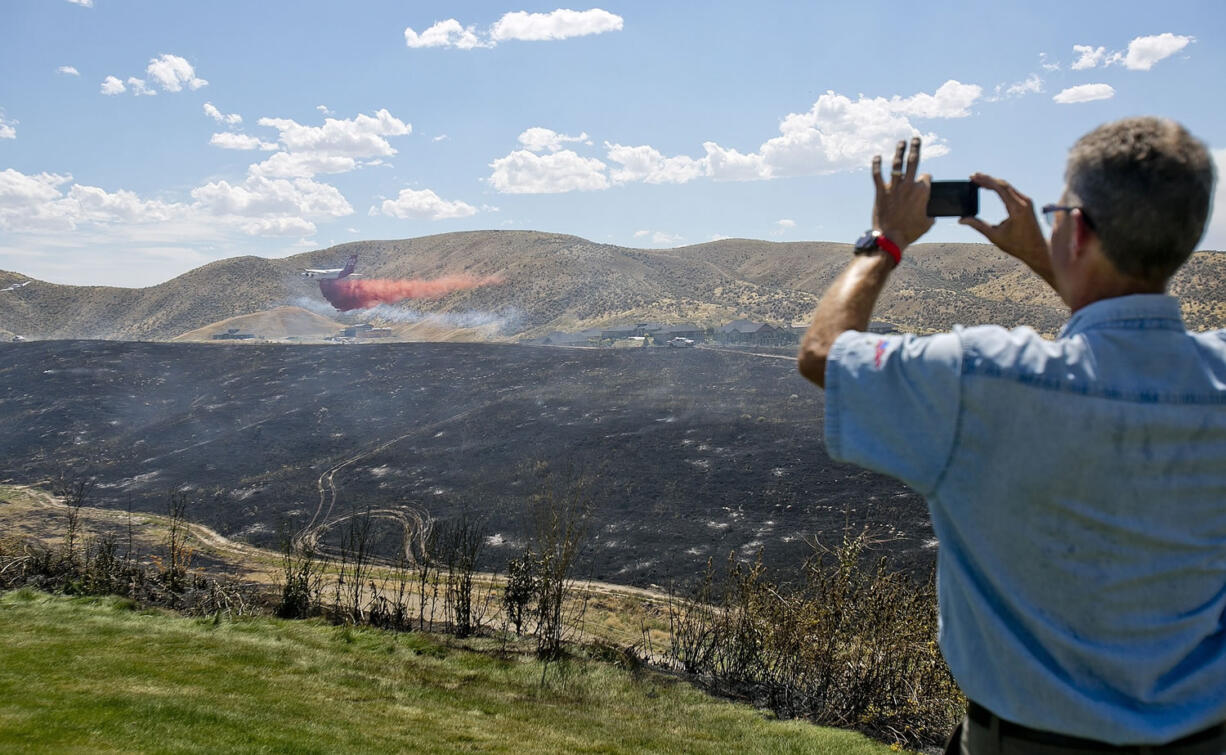 Douglas Tobin takes a photo of a plane dropping fire retardant near his house during a fire in the Boise, Idaho foothills on Thursday.