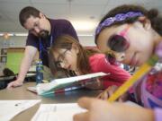 Substitute teacher and Washington State University Vancouver graduate Bryan Moxley helps fifth graders Anastazia McCusker, 11, center, and Monique Williams, 11, at Chief Umtuch Middle School on May 14, 2014.