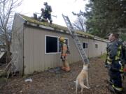 Firefighters ventilate the roof of a home on Tuesday after knocking out a fire inside the structure near the Vancouver Plaza shopping center.