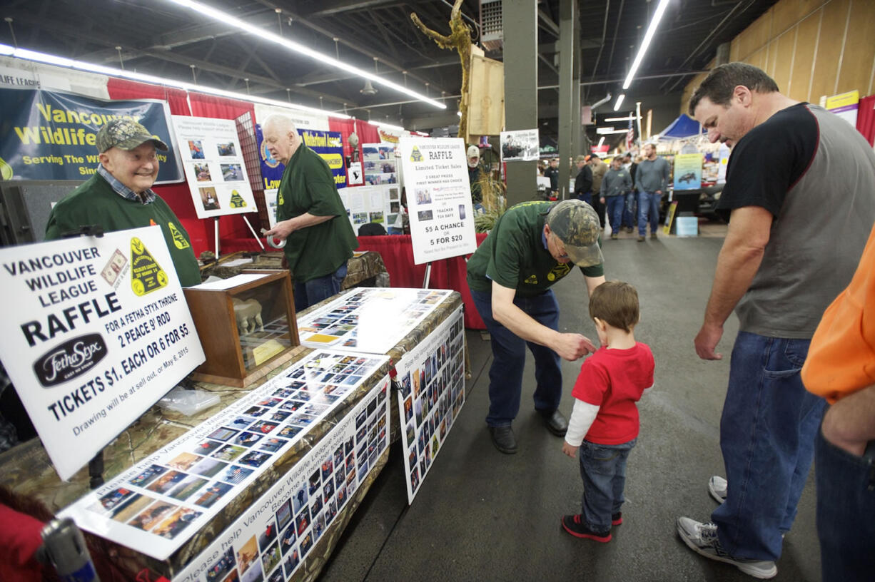 Chuck Sturm, left, and Russ Harris work in the Vancouver Wildlife League booth while Joe Sobolewski puts a decal on a young visitor at the Pacific Northwest Sportsmen's Show on Wednesday.