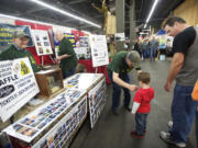 Chuck Sturm, left, and Russ Harris work in the Vancouver Wildlife League booth while Joe Sobolewski puts a decal on a young visitor at the Pacific Northwest Sportsmen's Show on Wednesday.