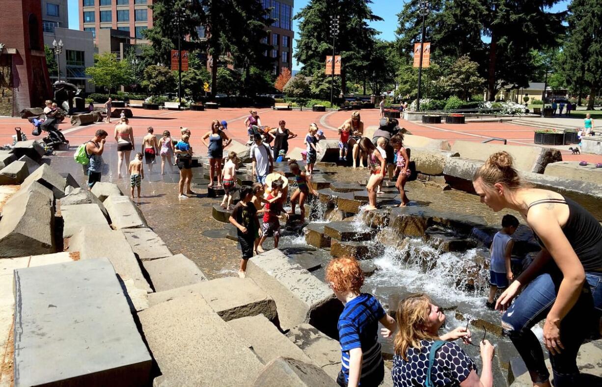 People take advantage of the hot weather and the fountains in Esther Short Park on Tuesday morning.