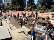 People take advantage of the hot weather and the fountains in Esther Short Park on Tuesday morning.