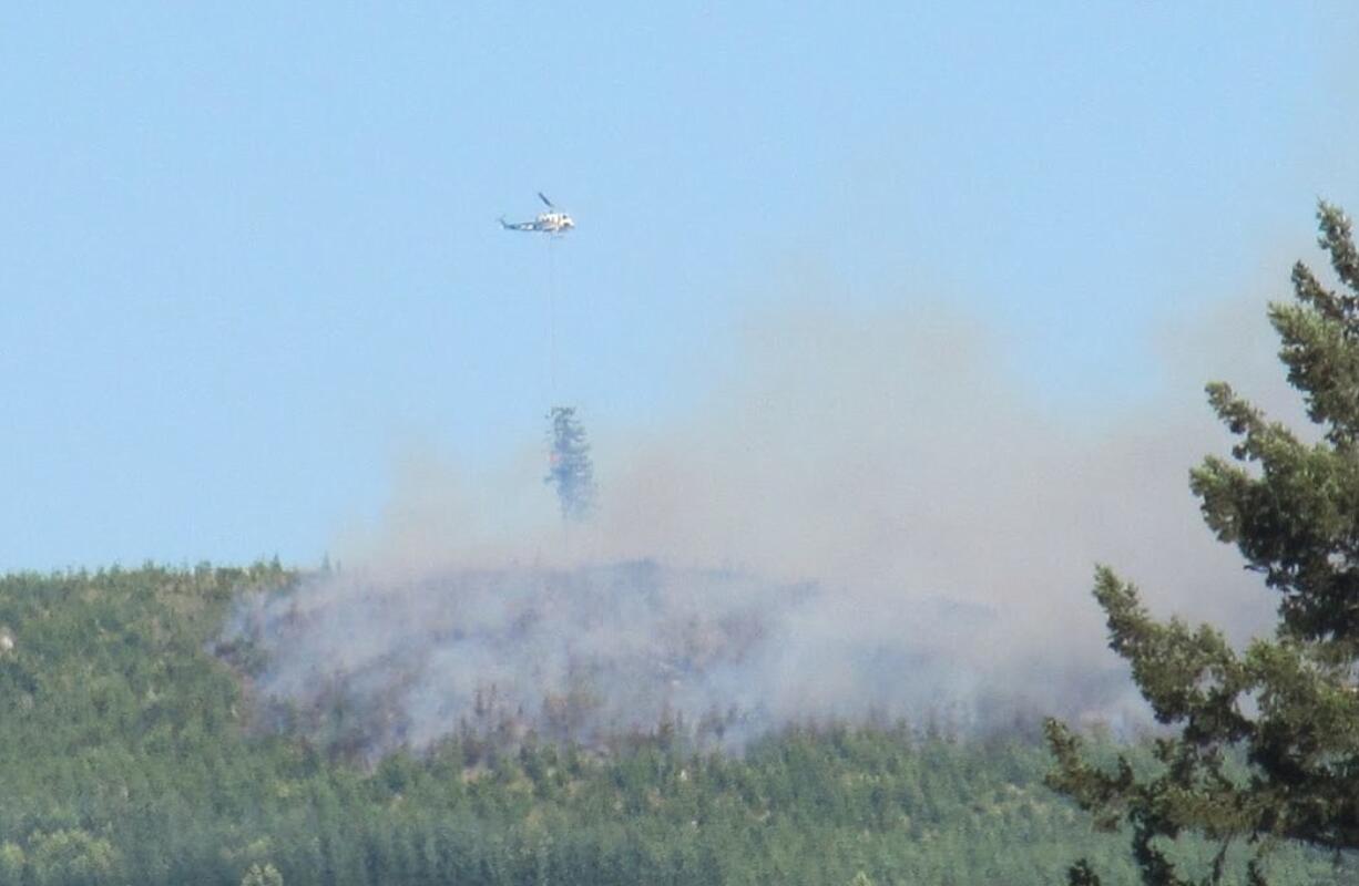 A helicopter makes a water drop on a wildfire burning Friday evening near the East Fork Lewis River near the mouth of Dole Valley in northeast Clark County.