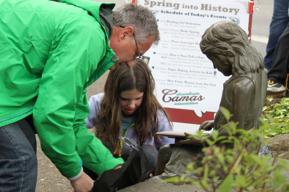 Grandfather and granddaughter, Randy Curtis and Olivia Brotherton, help remove the plastic from the newly refurbished reading girl statue. They spearheaded efforts to replace the statue's book, which was stolen more than a decade ago.