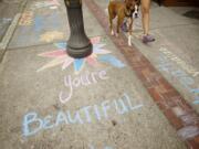 A pedestrian and her dog walk past an optimistic message in Uptown Village in Vancouver during the second annual Chalk the Walks, a project of the Joy Team.