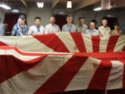 A group of visitors from the Northwest and members of a Japanese historical society unfold a flag that once flew from the Japanese battleship Asahi. An American Marine took it as a war trophy after World War II.