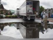 Brian Alan of Performance Food Group is reflected in a puddle in the parking lot of Joe’s Crab Shack in Vancouver as he drops off a load for the restaurant Thursday morning. Residents, workers and commuters dealt with slick streets and rainy conditions earlier in the morning as wet weather blanketed the area.