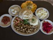 A chicken shawarma dinner, center, is served at the Pita House in Battle Ground along with house spicy sauce, clockwise from bottom left, house potato salad, pistachio baklava, green cabbage and red cabbage.