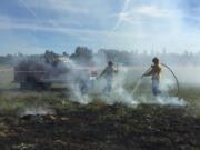 Clark County Fire & RescueFirefighters spray down a grass fire in a field west of Battle Ground on Tuesday afternoon.