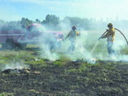 Firefighters spray down a grass fire in a field west of Battle Ground Tuesday afternoon.