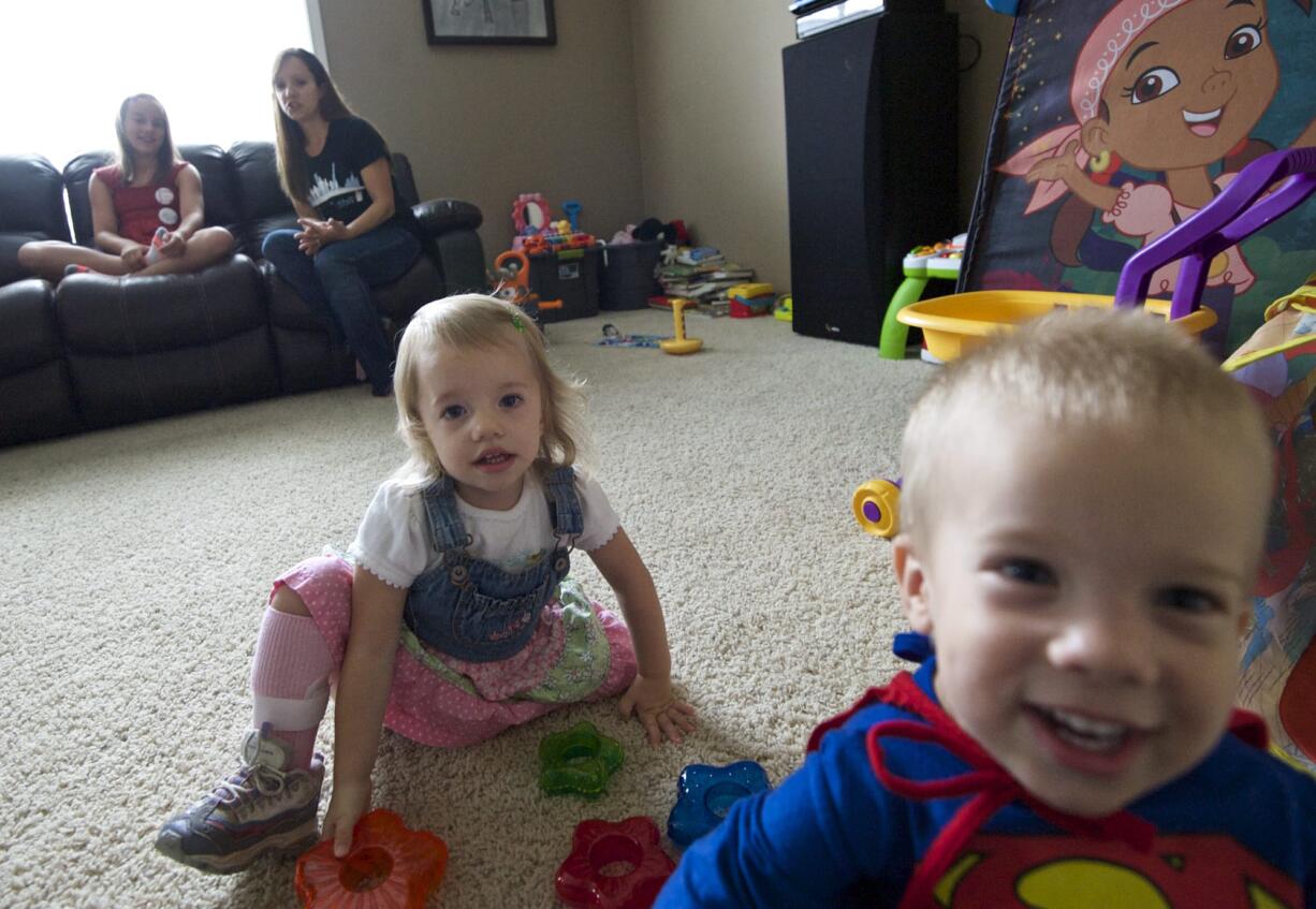 Ronda Jensen sits with her daughter Lilly, 9, as her 2-year-old twins, Gus and Eva, play on the living room in their Ridgefield home.