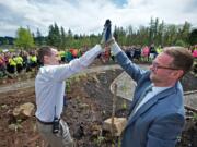 Skyridge Middle School Associate Principal Clint Williams, left, and Principal Aaron Smith give each other a high-five Tuesday after planting two camas lilies, signifying the completion of the Skyridge Lewis and Clark native plant garden, during a ceremony coinciding with Earth Day.