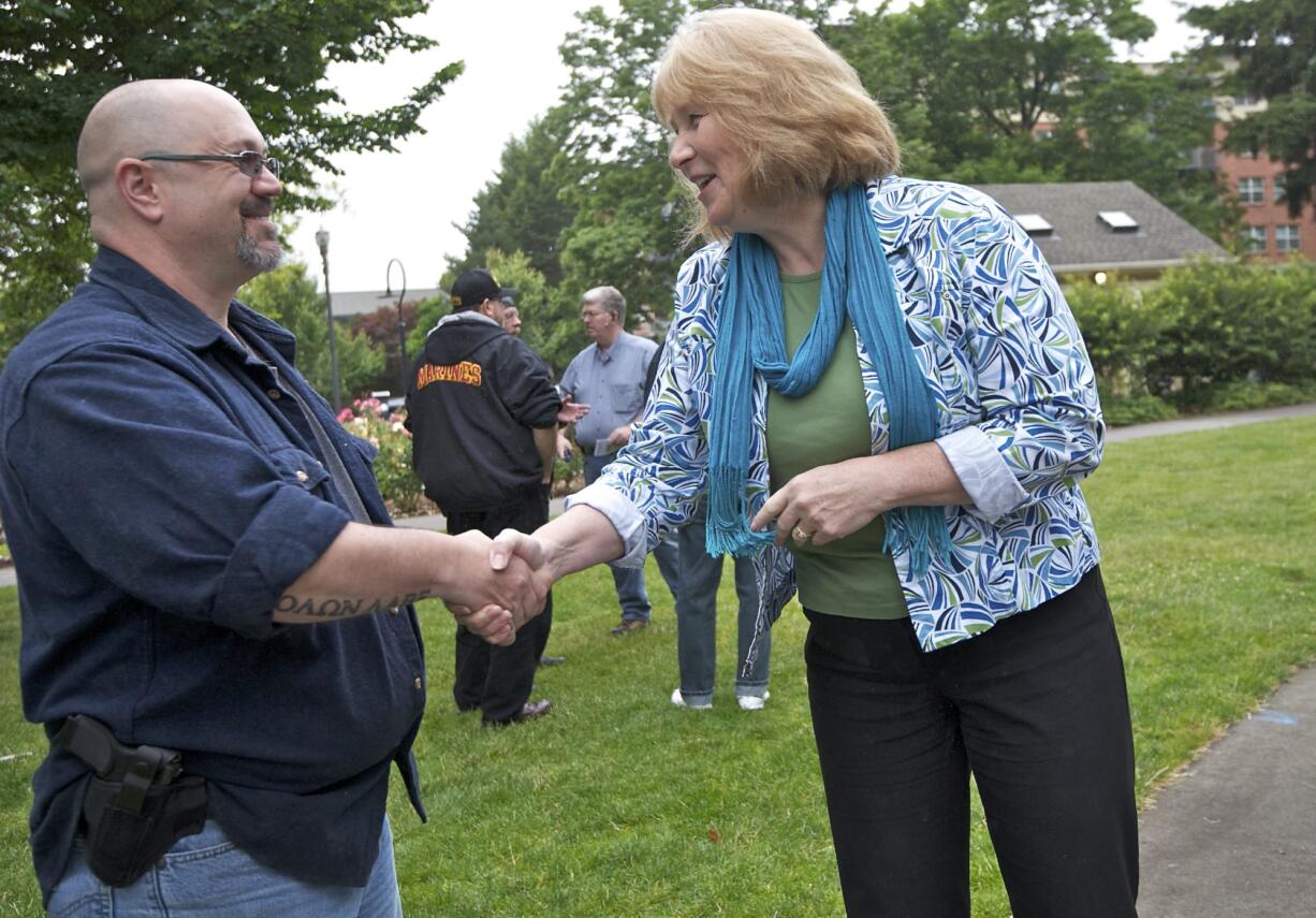 Open-carry gun activist Larry White and gun safety advocate and Vancouver City Councilwoman Anne McEnerny-Ogle shake hands as the two groups hold their separate rallies at Esther Short Park on Tuesday. McEnerny-Ogle was one of the few people who crossed camps to interact with the other group.