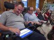 Brian Epp, left, uses a tablet to communicate with John Meyer of Camas at the regional ALS Association support group's Christmas potluck Wednesday at St. Luke's Episcopal Church in Vancouver.