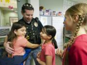 Vancouver police Detective Adam Millard receives a hug from third-grader Berenice Pintor, 9, left, and Maritza Sanchez, 9, on Friday before spring break at Fruit Valley Elementary School.