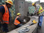 City of Vancouver workers Tony Castro, from left, Tracy Livingston and Kevin Battan prepare to install a motion-sensor light next to the Mill Plain Boulevard sound wall Friday to deter illegal activities in the alcoves.