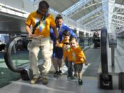 Saul Martinez Class, left, assists Owen Martinez with Catharine Hunter and Joshua Martinez, right, on the moving walkway at PDX at an event where families with children with autism could practice boarding a plane.