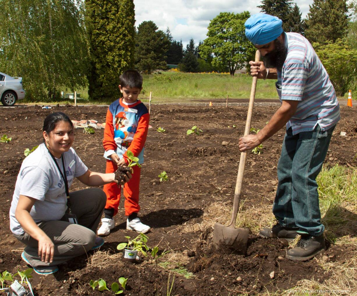 Harpal Kaur, left, preschooler Satraj Singh and Lakhbinder Singh help plant a new community garden on May 10 at Orchards Elementary School. Along with the family, nearly 200 other volunteers came out to clean up the property by the school's parking lot, which will now be used as an outdoor classroom and community garden.