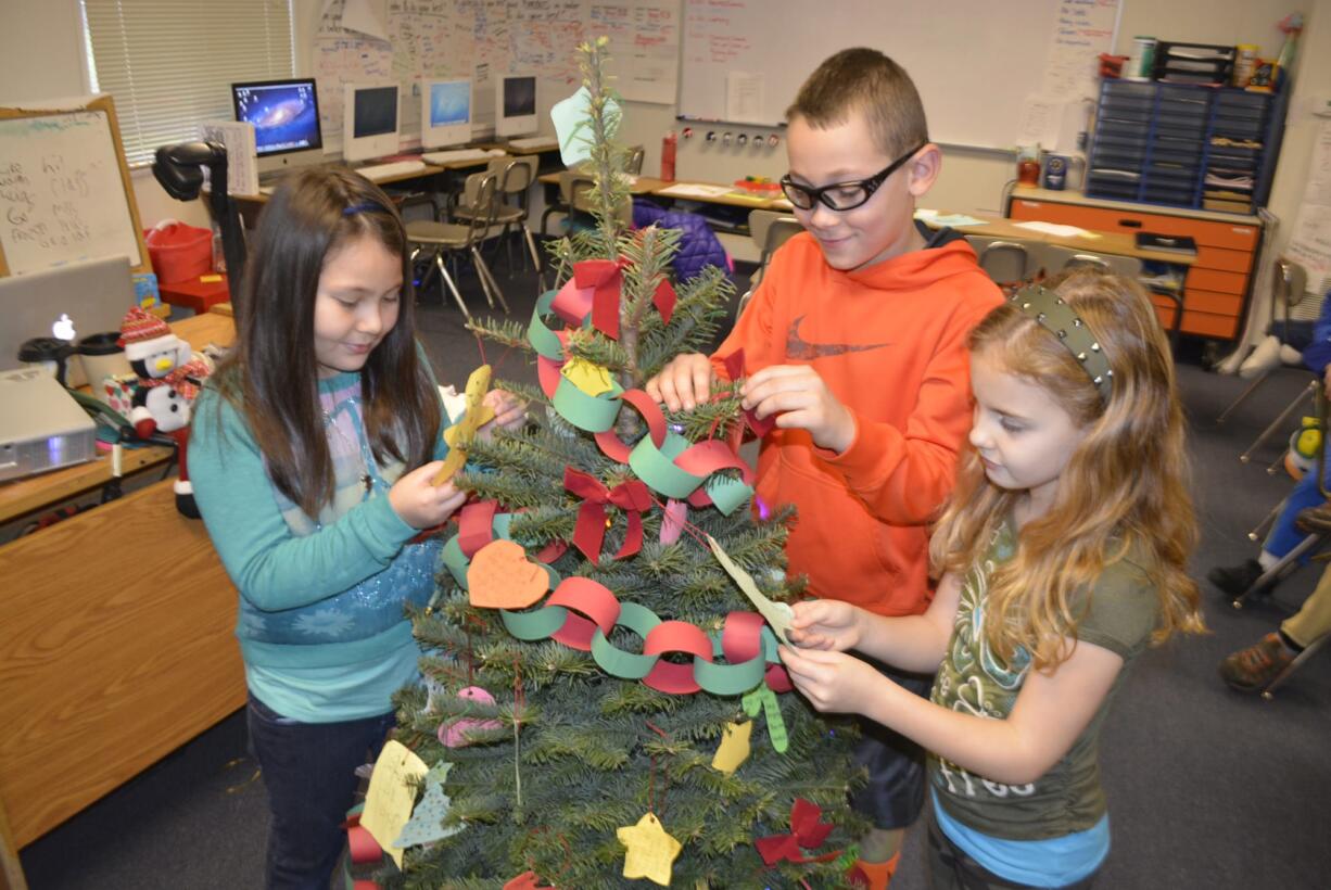 Washougal: Cape Horn-Skye Elementary School third-graders Ellison Wilkins, from left, Holden Bea and Avery Berg decorate a Christmas tree with paper ornaments with inspirational quotes for their classes holiday project.