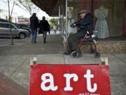 Painter and Southwest Washington Watercolor Society member John Beckman, 86, waits for a ride near a sign directing people to Gallery 360 at Main and Ninth streets during First Friday Downtown art walk.