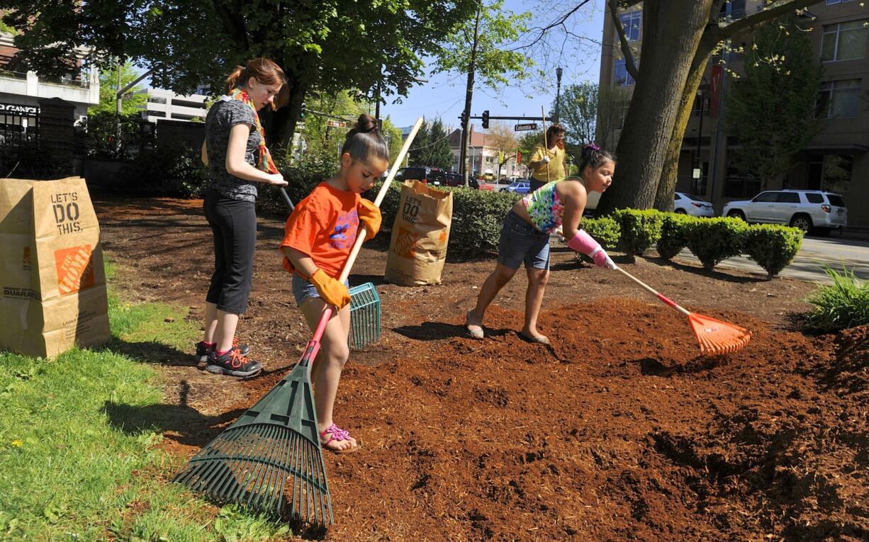 Nevaeh Jackson, right, Cherakee Elliott, left, and Oddessa Riley rake bark dust Saturday as part of a cleanup of Esther Short Park.