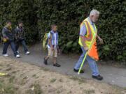 Volunteer Mick Hawthorn escorts Trevor Watts, his brother Owen and Aderris Bantilan, from left, to Washington Elementary via East 33rd Street on Wednesday morning.