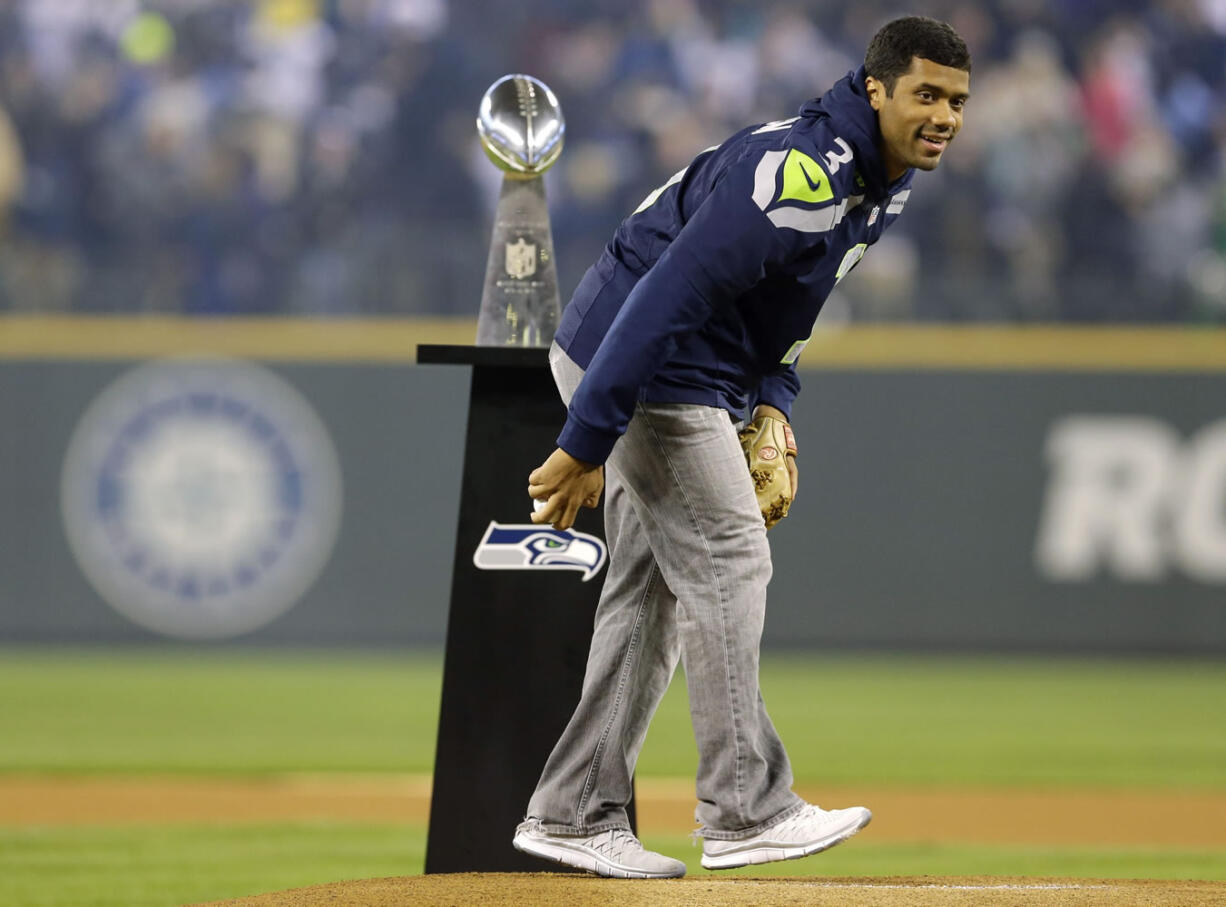 Seattle Seahawks quarterback Russell Wilson stands by the Vince Lombardi Trophy as he winds up to throw the ceremonial first pitch Tuesday at the Seattle Mariners' baseball home-opener.